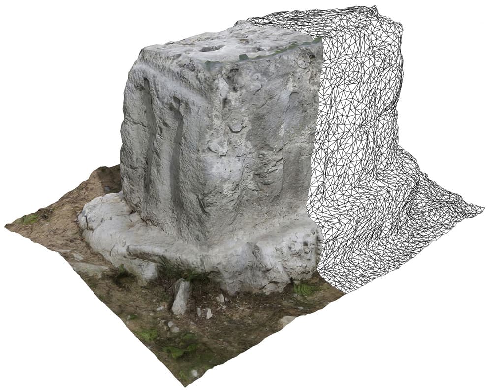 A digital representation of a partially completed 3D scan of a stone cube with detailed carvings on its surface. The scan visualized as a wireframe mesh extends from the actual stone, illustrating the process of digitizing a physical object into a 3D model.