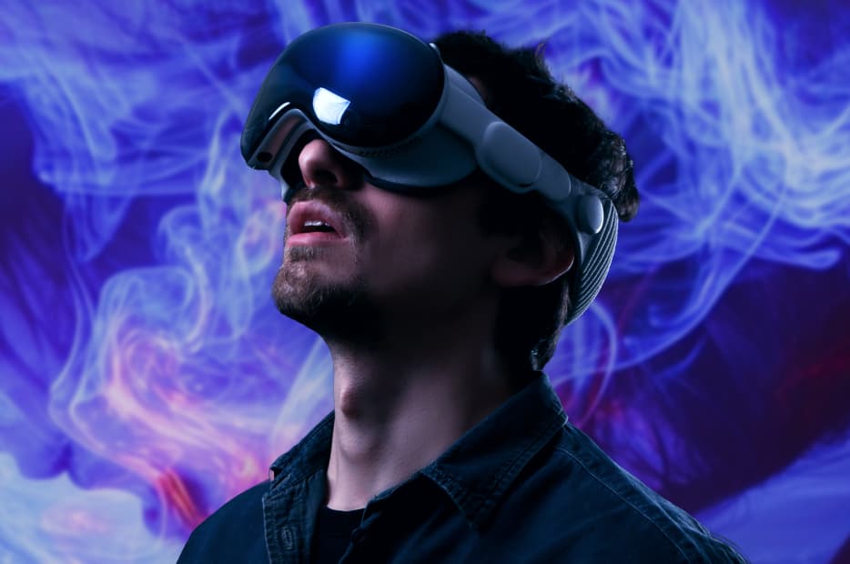 A man wearing a VR headset looks up, immersed in a virtual experience, with dynamic blue and purple smoke-like effects in the background.