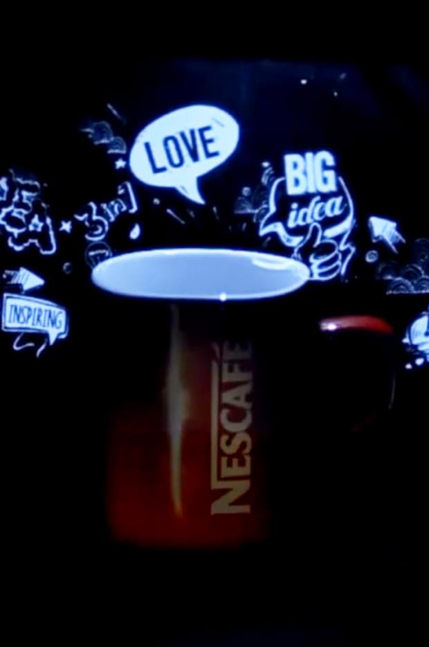 A close-up of a coffee cup with animated drawings and words like 'LOVE' and 'BIG idea' projected onto it, illustrating creative advertising or digital art.