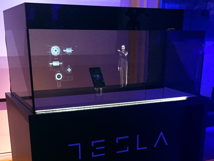 A presentation at a tech expo featuring a life-sized holographic display of a speaker next to a physical lectern, indicating an advanced, immersive experience for the audience.
