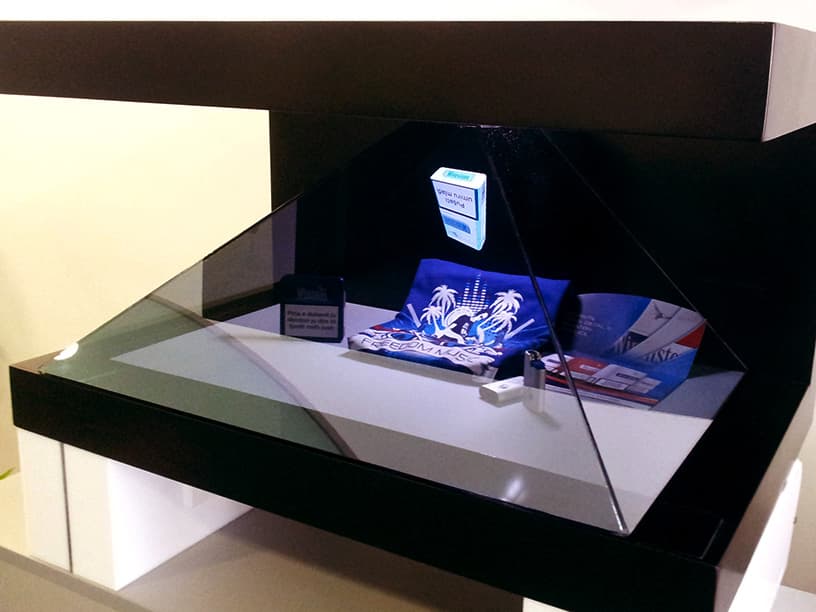 An angled view of a museum display case illuminated from within, showcasing a holographic projection of a blue and white digital artifact, combining traditional exhibit methods with modern technology.