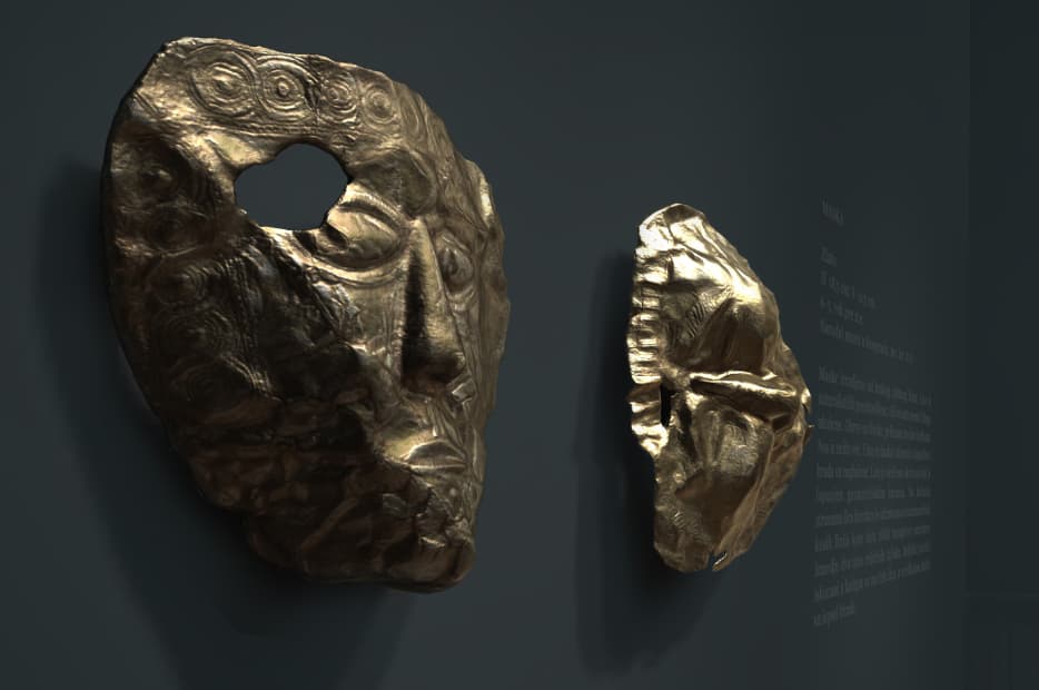 Two halves of a broken ancient bronze mask, featuring a stylized human face with detailed engraving, displayed side by side against a dark background.