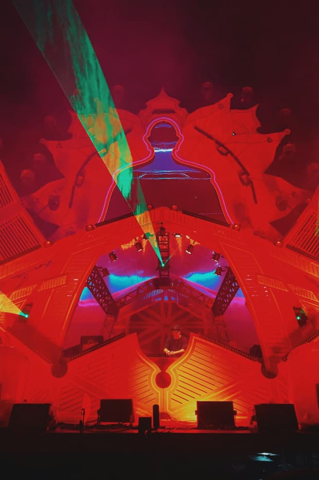 A dramatic stage at a music festival, with vibrant laser lights and neon outlines of a human figure, creating an electrifying atmosphere for a live performance.