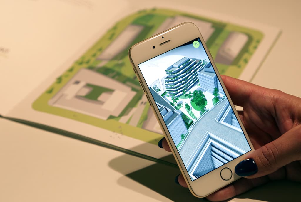 A smartphone held over a paper, displaying an augmented reality image of a building