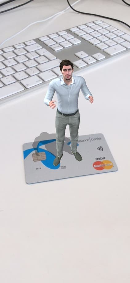 An augmented reality (AR) depiction of a small, animated figure of a man standing on top of a credit card, next to a keyboard, indicating a visualization of personal finance and an online banking services.